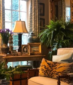 a living room filled with lots of furniture and plants on top of a table next to a window