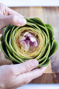 a person holding an artichoke on top of a wooden cutting board