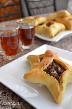 two white plates topped with pastries on top of a table next to glasses of tea