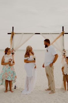 a group of people standing on top of a beach next to each other under a white canopy