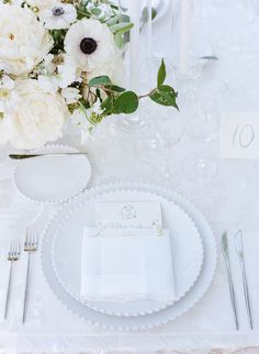 a white table setting with flowers and silverware