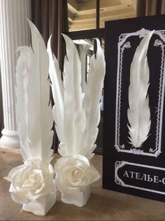 two vases with white flowers and feathers on them next to a sign that says atelle - co