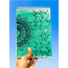 a hand holding up a spiral notebook with an image of leaves on the cover and blue sky in the background