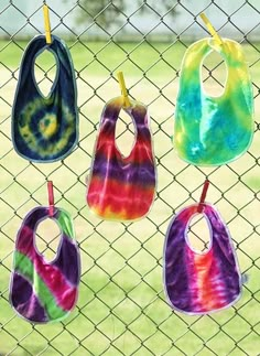 six bibs hanging on a chain link fence with grass in the backround