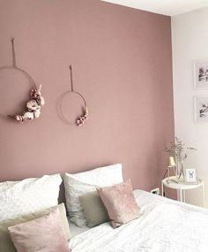 a bedroom with pink walls and white bedding, two hanging decorations on the wall