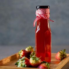 a bottle filled with liquid sitting on top of a wooden tray next to strawberries