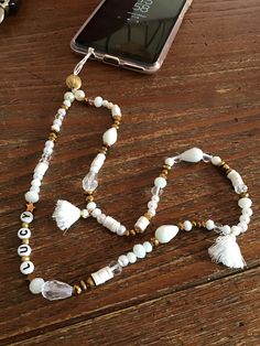 a cell phone laying on top of a wooden table next to a beaded necklace