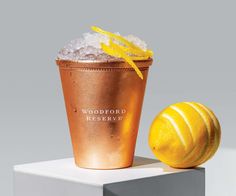 a gold cup with ice and a lemon on top sitting on a white pedestal next to it