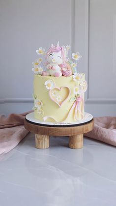 a yellow cake with white flowers and a unicorn on top is sitting on a wooden stand