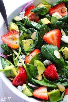 a white bowl filled with spinach, strawberries and avocado on top