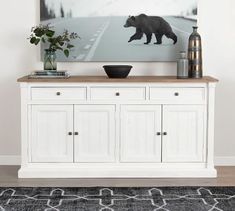 a white cabinet with two vases and a bear painting on the wall above it