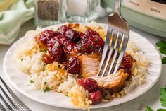 a white plate topped with rice and meat covered in cranberry sauce next to a fork