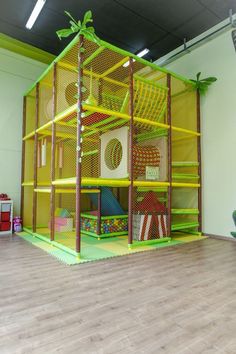 an indoor play area with yellow and green mesh walls, wooden flooring and toys