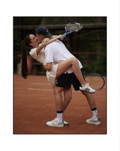 a man and woman hug while holding tennis racquets on a clay court