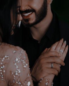 a man and woman holding each other with their hands in front of them, smiling at the camera