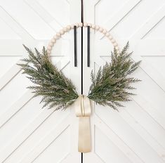 a wreath hanging on the side of a white door with two wooden beads and some greenery