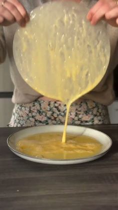 a woman pouring batter on top of a bowl filled with yellow liquid in front of her