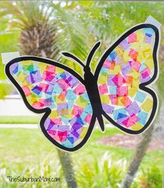 a butterfly made out of colored paper sitting on top of a window sill in front of a palm tree