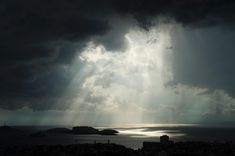 the sun shines through dark clouds over an island and body of water in the distance