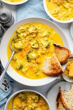 two bowls of soup with broccoli and bread on the side, next to silver spoons