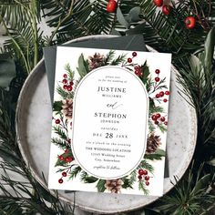 a white wedding card with pine cones and berries on it, surrounded by greenery