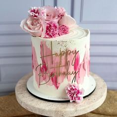 a birthday cake decorated with pink flowers and gold lettering that says happy birthday on it