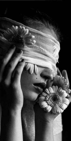 a black and white photo of a woman covering her eyes with flowers in front of her face