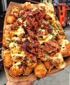 a person holding up a pizza covered in cheese and bacon