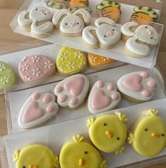 several decorated cookies in plastic boxes on a wooden table, one with yellow and pink frosting