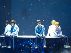 four young men sitting on top of a bench in front of a blue wall with stars