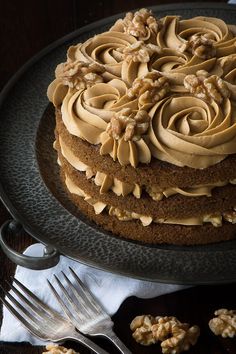 a chocolate cake with walnuts and frosting on a black plate next to silverware