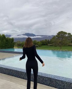 a woman standing in front of a pool with her back to the camera, wearing black