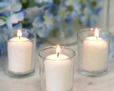 three lit candles sitting on top of a table next to blue and white flowers in vases