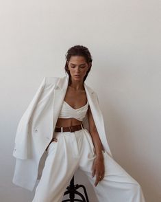 a woman sitting on top of a chair wearing white pants and a blazer jacket