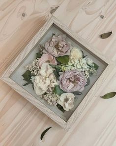 an old frame with flowers in it sitting on a wooden table next to leaves and scissors