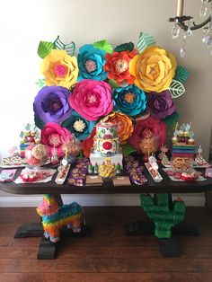 a table topped with lots of colorful paper flowers and desserts on top of it