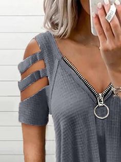 a woman taking a selfie while wearing a gray top with cut out sleeves and silver bracelets