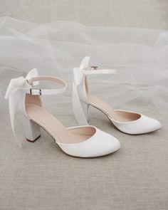 a pair of white high heeled shoes with a bow