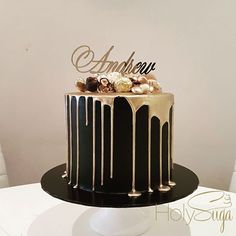 a black and gold cake with white frosting is on top of a table in front of a white wall