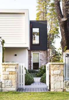 a house with a white fence and trees in the front yard, along with a brick walkway leading to it