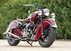 a red motorcycle is parked in front of some bushes