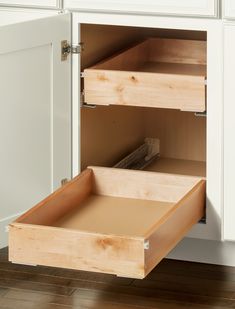 an open drawer in a kitchen with white cabinets and wooden drawers on the bottom shelf