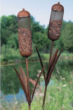 two metal bird feeders sitting next to each other on top of a grass covered field