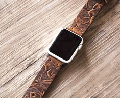 an apple watch band with flowers and leaves on it, sitting on a wooden surface