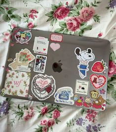 an open laptop computer sitting on top of a bed covered in stickers