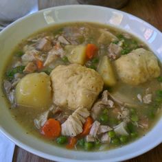 a white bowl filled with chicken and dumpling soup on top of a wooden table