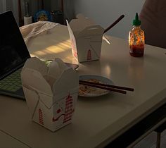 an open laptop computer sitting on top of a table next to some boxes and chopsticks