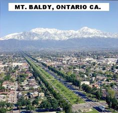 an aerial view of a city with snow capped mountains in the background and text overlay that reads mt baldy, ontario ca