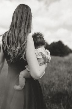 a woman holding a baby in her arms while walking through a field with other people