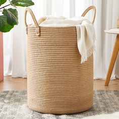 a large round basket with handles on the floor next to a potted plant